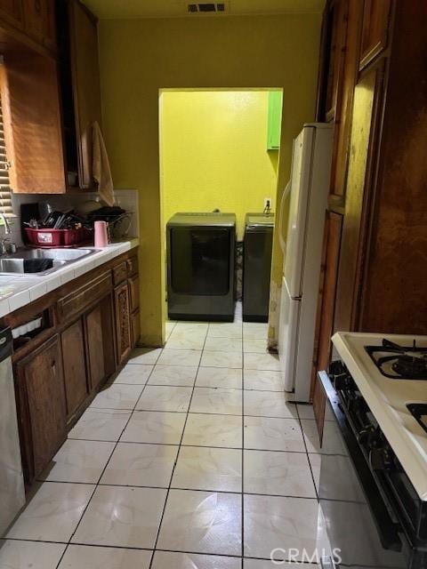 kitchen with sink, separate washer and dryer, tile countertops, white appliances, and light tile patterned floors