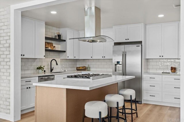 kitchen with island exhaust hood, a kitchen bar, stainless steel appliances, white cabinets, and a kitchen island