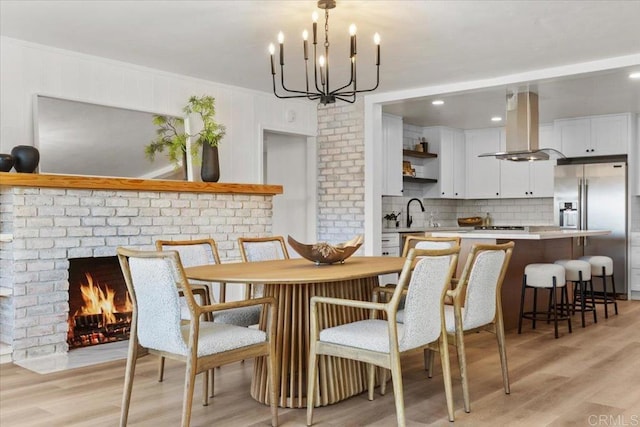 dining room with ornamental molding, light wood-type flooring, a fireplace, and a chandelier