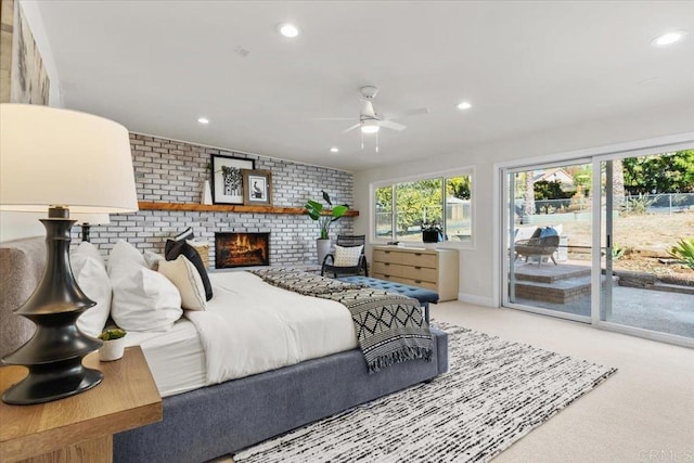 bedroom with access to exterior, ceiling fan, a brick fireplace, brick wall, and light colored carpet