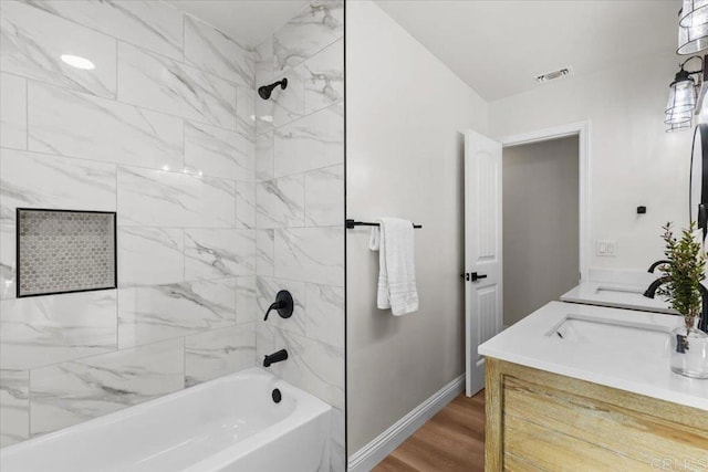 bathroom with hardwood / wood-style floors, tiled shower / bath combo, and vanity