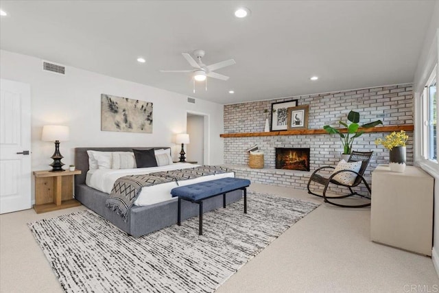 bedroom with ceiling fan, a fireplace, light colored carpet, and brick wall