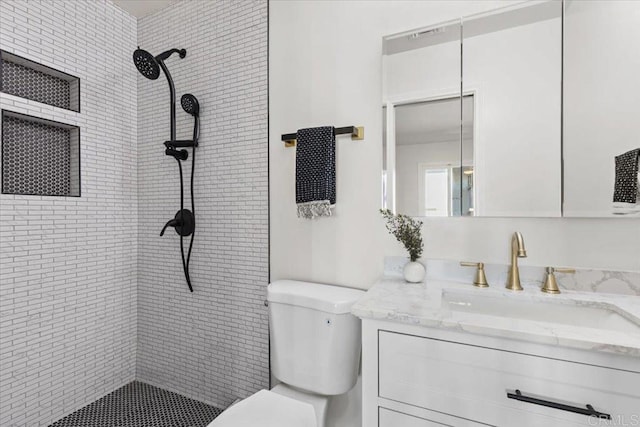 bathroom featuring a tile shower, vanity, and toilet