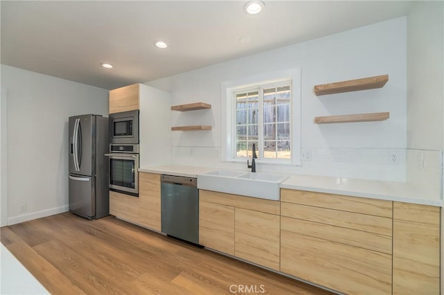 kitchen with stainless steel appliances, sink, light hardwood / wood-style flooring, and light brown cabinets