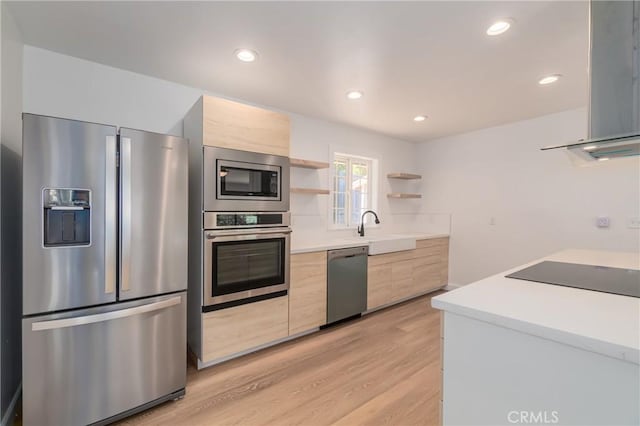 kitchen featuring stainless steel appliances, sink, wall chimney range hood, and light wood-type flooring