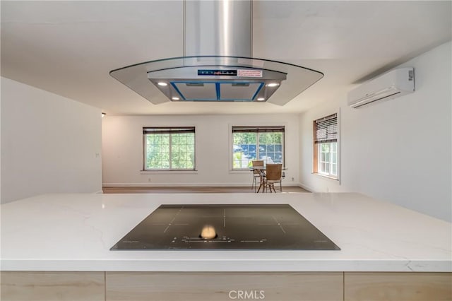 kitchen with black electric stovetop, a wall mounted AC, light stone countertops, and light brown cabinets