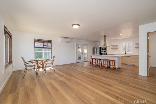 interior space with a kitchen breakfast bar, stainless steel appliances, a center island, a wall mounted AC, and light hardwood / wood-style floors