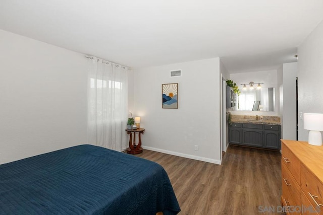 bedroom with sink, ensuite bath, and dark wood-type flooring