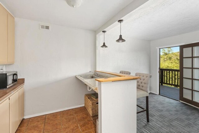 kitchen with pendant lighting, sink, a kitchen bar, kitchen peninsula, and cream cabinets