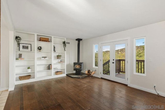 unfurnished room featuring built in shelves, dark wood-type flooring, french doors, and a wood stove