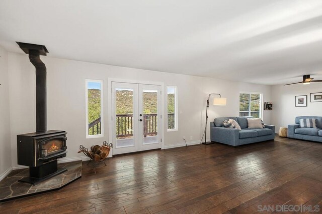 living room featuring a wood stove, dark wood-type flooring, ceiling fan, and french doors