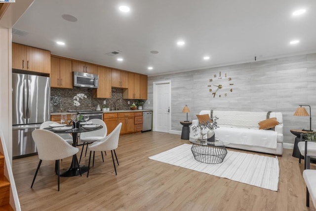 kitchen with appliances with stainless steel finishes, backsplash, light hardwood / wood-style floors, and sink