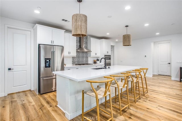 kitchen featuring pendant lighting, a kitchen island with sink, wall chimney exhaust hood, light hardwood / wood-style floors, and stainless steel appliances