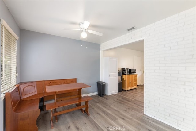 dining space with ceiling fan, brick wall, and light hardwood / wood-style flooring