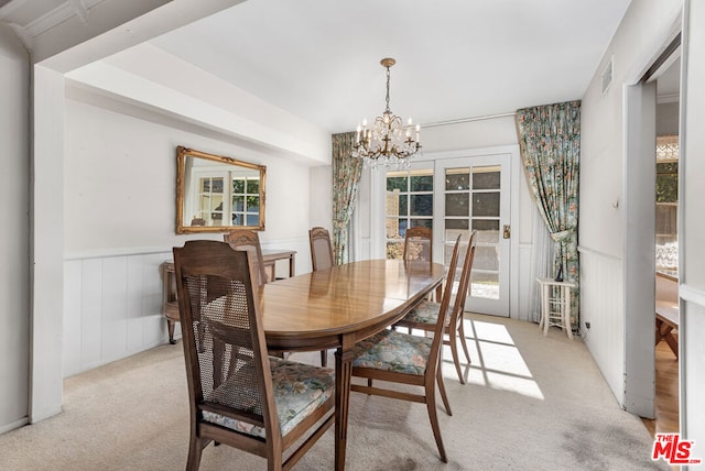 dining room with wood walls, light carpet, a wealth of natural light, and an inviting chandelier