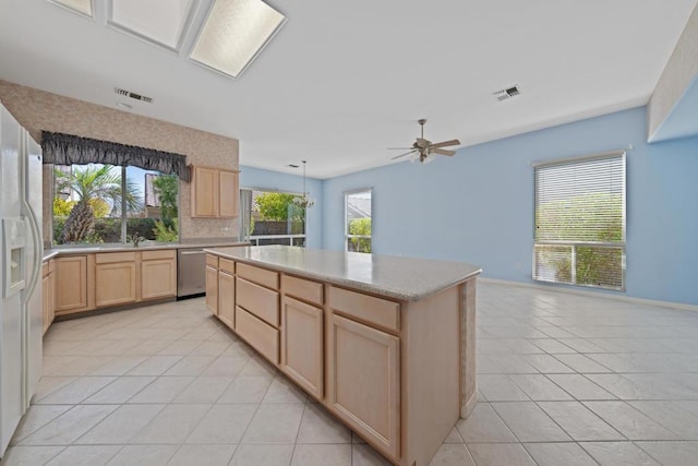 kitchen featuring stainless steel dishwasher, a healthy amount of sunlight, light tile patterned floors, and light brown cabinets