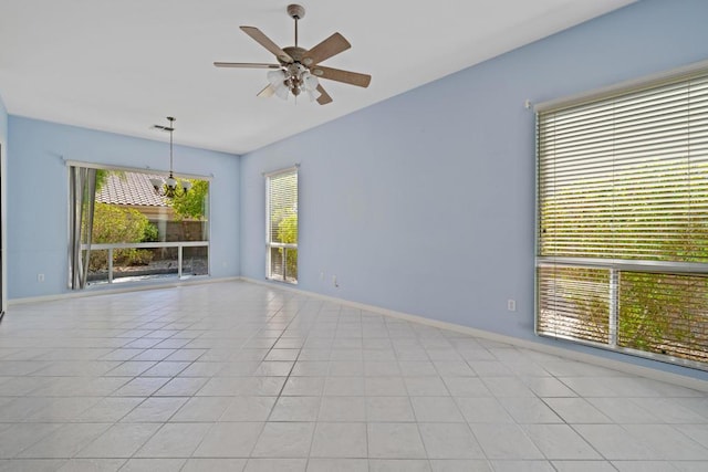 tiled spare room featuring plenty of natural light and ceiling fan with notable chandelier