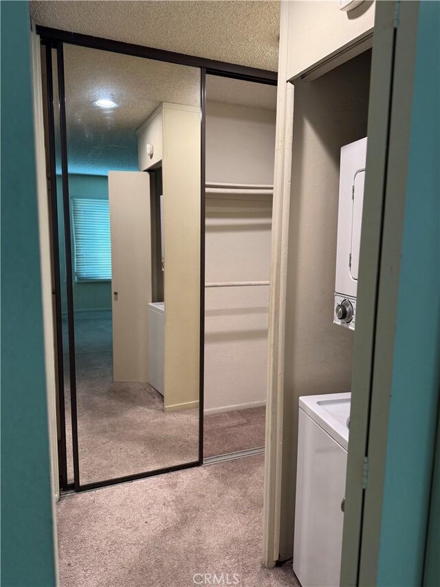 laundry area featuring stacked washer and clothes dryer, light carpet, and a textured ceiling