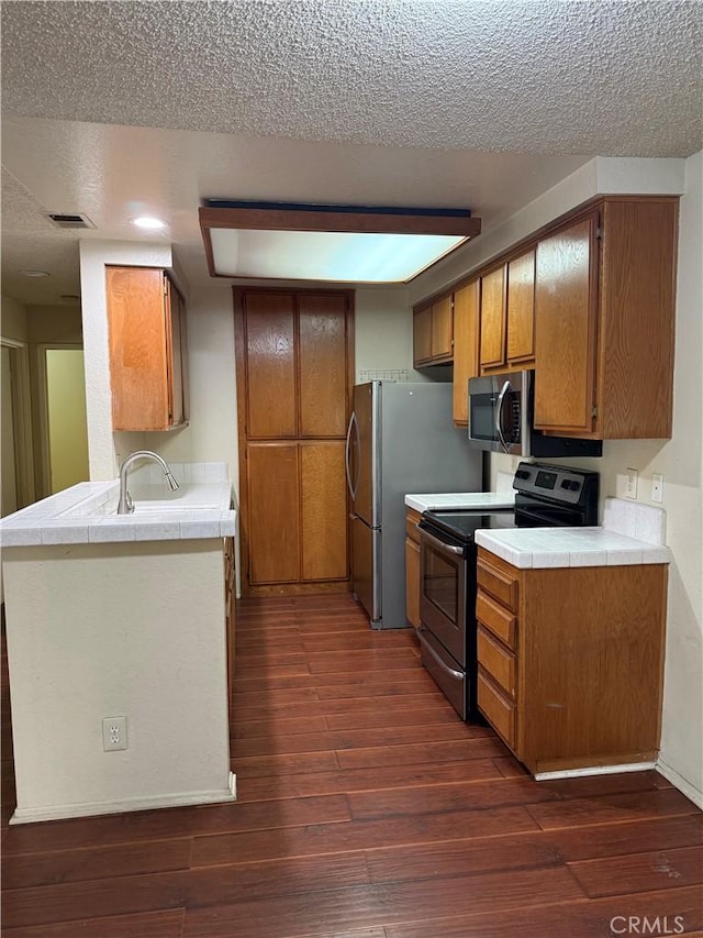 kitchen featuring sink, dark wood-type flooring, stainless steel appliances, a textured ceiling, and kitchen peninsula