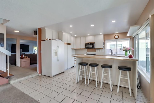 kitchen with white refrigerator with ice dispenser, light carpet, sink, a kitchen bar, and white cabinetry