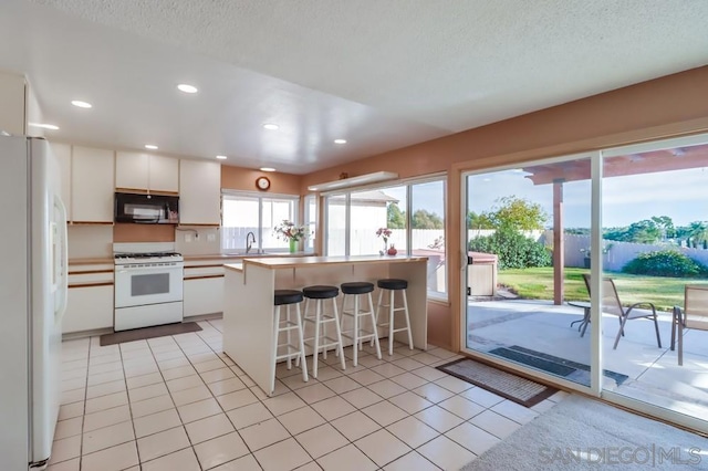 kitchen with a kitchen breakfast bar, white appliances, sink, light tile patterned floors, and white cabinetry