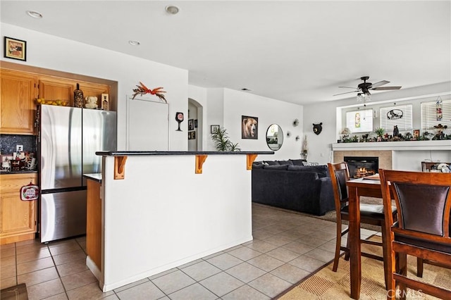 kitchen with stainless steel refrigerator, ceiling fan, a breakfast bar, a fireplace, and light tile patterned floors