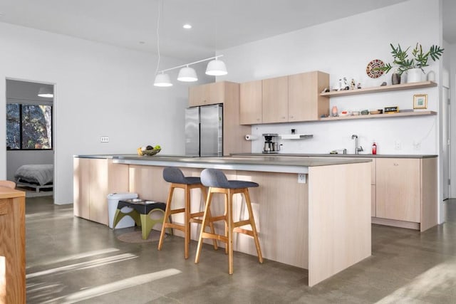 kitchen with a breakfast bar, light brown cabinetry, a center island, stainless steel refrigerator, and pendant lighting