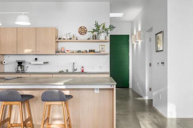 kitchen featuring a kitchen breakfast bar, sink, light brown cabinetry, and decorative light fixtures