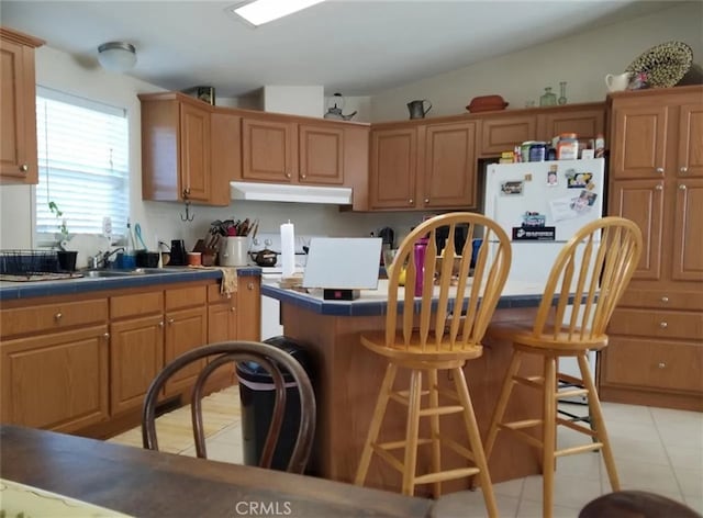 kitchen with a breakfast bar, vaulted ceiling, sink, light tile patterned floors, and white refrigerator