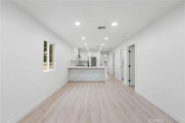 kitchen with stainless steel refrigerator, kitchen peninsula, white cabinets, and light hardwood / wood-style floors