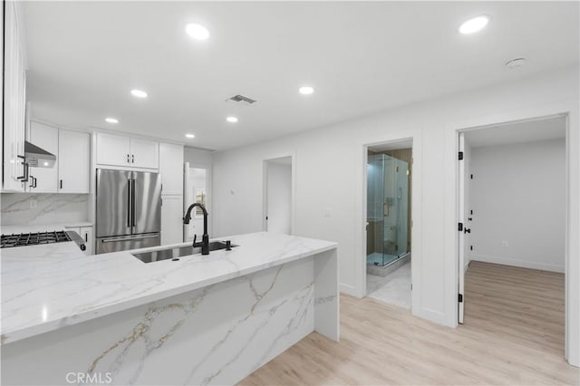 kitchen with light stone countertops, appliances with stainless steel finishes, sink, light hardwood / wood-style flooring, and white cabinetry