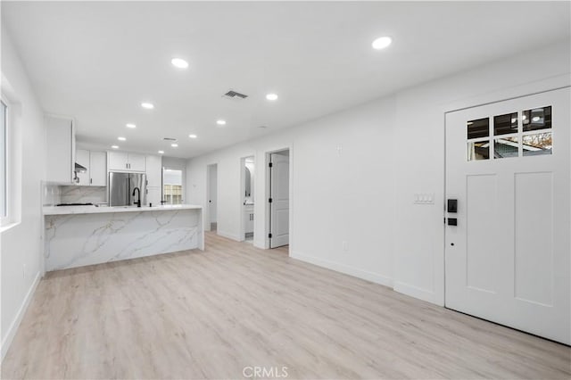 interior space featuring white cabinetry, tasteful backsplash, kitchen peninsula, stainless steel fridge, and light wood-type flooring