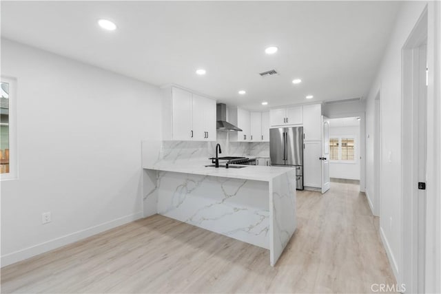 kitchen with kitchen peninsula, appliances with stainless steel finishes, light wood-type flooring, wall chimney range hood, and white cabinetry