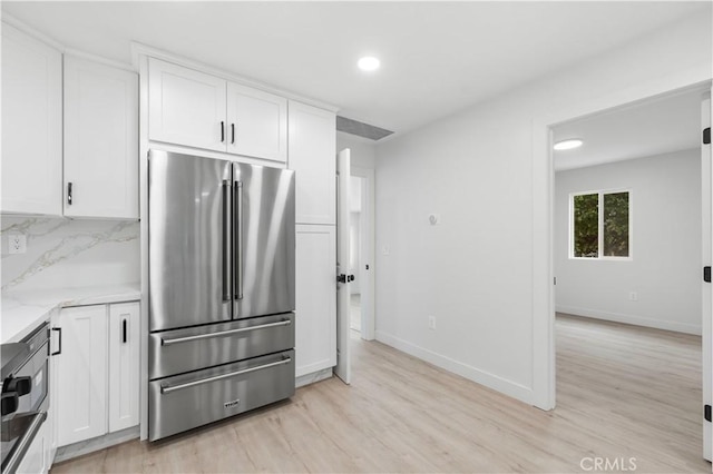 kitchen with white cabinetry, high end refrigerator, light stone countertops, and light hardwood / wood-style floors