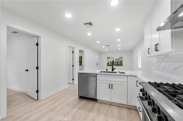 kitchen with kitchen peninsula, wall chimney exhaust hood, stainless steel appliances, sink, and white cabinetry