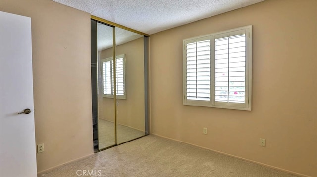 unfurnished bedroom featuring a textured ceiling, light carpet, and a closet