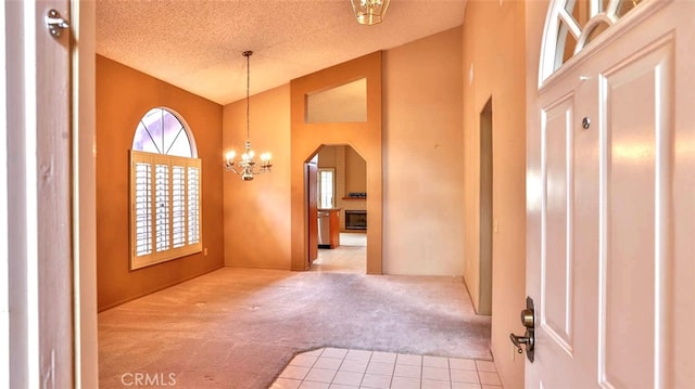 entrance foyer with carpet flooring, a textured ceiling, high vaulted ceiling, and a chandelier