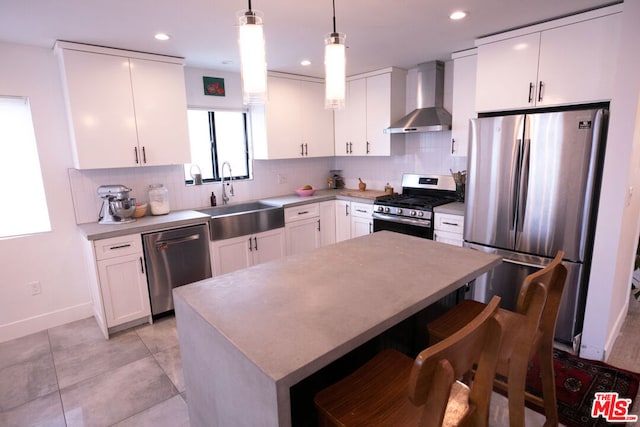 kitchen with white cabinetry, sink, wall chimney exhaust hood, hanging light fixtures, and stainless steel appliances