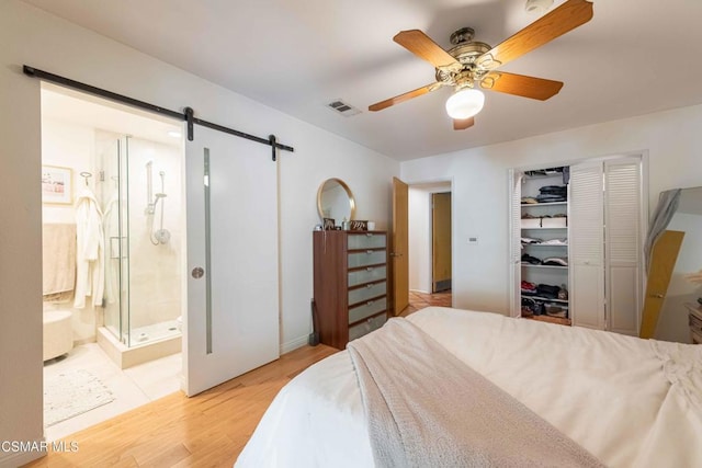 bedroom featuring connected bathroom, a closet, ceiling fan, light hardwood / wood-style flooring, and a barn door