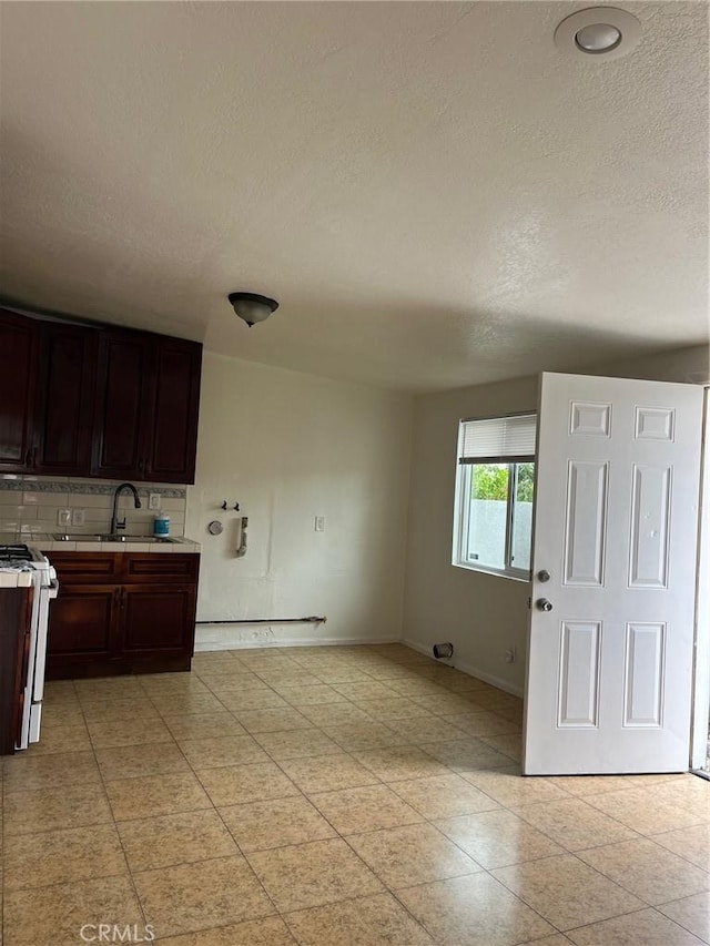 kitchen with sink, tasteful backsplash, white range, a textured ceiling, and dark brown cabinets