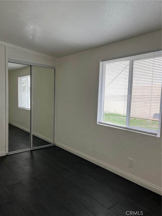 unfurnished bedroom with dark hardwood / wood-style floors, multiple windows, and a closet