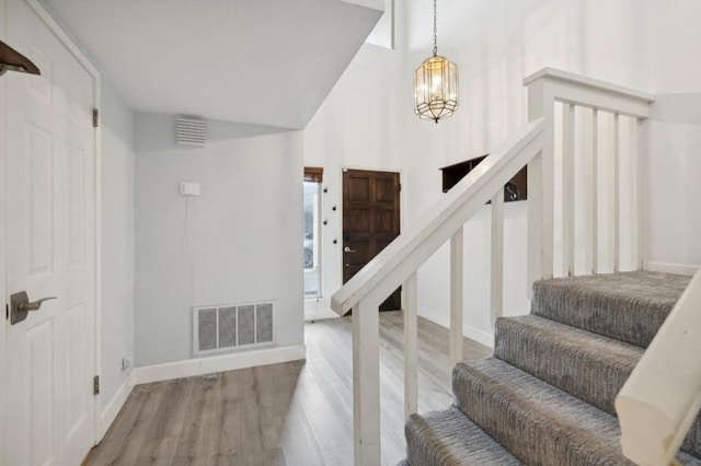 stairway with an inviting chandelier, hardwood / wood-style floors, and a towering ceiling