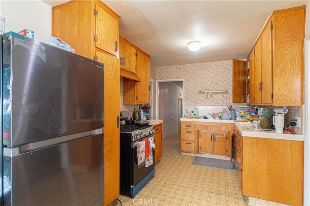 kitchen featuring black gas range oven, tasteful backsplash, stainless steel refrigerator, and sink