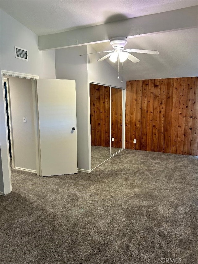 unfurnished bedroom with wood walls, lofted ceiling, dark colored carpet, ceiling fan, and a textured ceiling