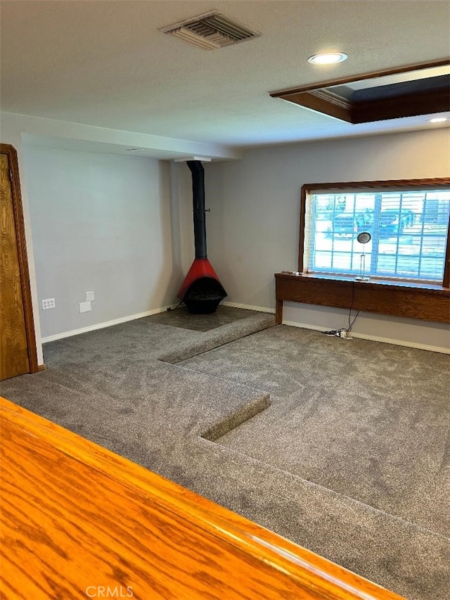 spare room featuring carpet floors, ornamental molding, a tray ceiling, and a wood stove