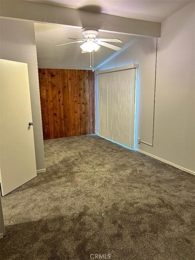 unfurnished bedroom with carpet flooring, ceiling fan, beamed ceiling, and wood walls