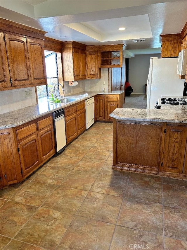 kitchen with white appliances, a raised ceiling, sink, decorative backsplash, and light stone counters