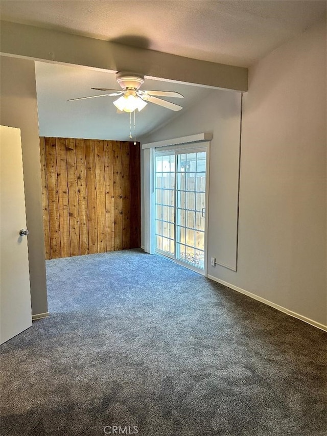 spare room featuring ceiling fan, lofted ceiling with beams, wood walls, and dark carpet