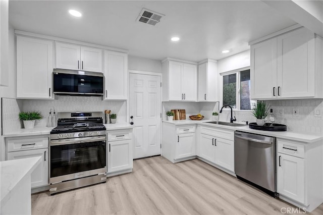 kitchen featuring white cabinets, sink, light hardwood / wood-style flooring, appliances with stainless steel finishes, and tasteful backsplash