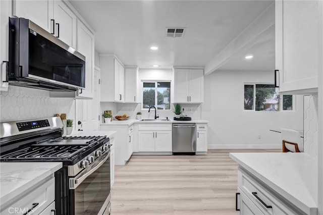 kitchen featuring backsplash, white cabinets, light hardwood / wood-style flooring, light stone countertops, and stainless steel appliances